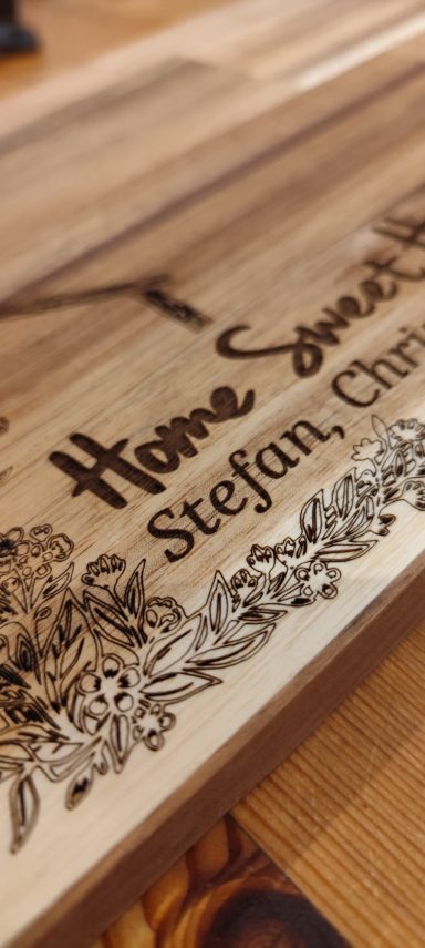 Gravierte Holzplatte mit dem Text "Home Sweet Home" und floralem Dekor.