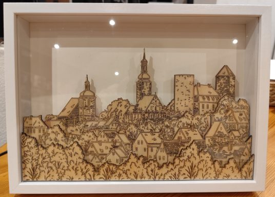 Detailreiche Holzschnitt-Darstellung einer Stadtlandschaft in einem Rahmen.