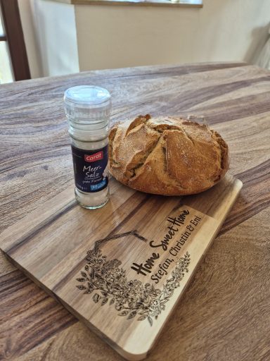 Ein Brotlaib auf einem Holzbrett neben einem Glas mit Salz.